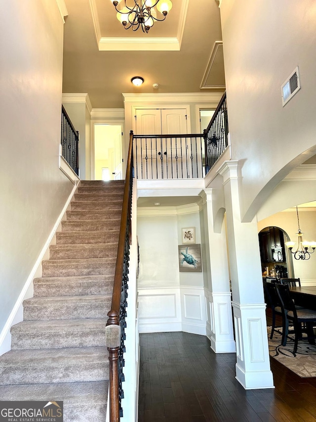 stairs with a chandelier, ornamental molding, hardwood / wood-style floors, and a decorative wall