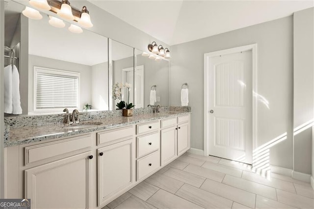 full bath featuring double vanity, baseboards, a sink, and lofted ceiling