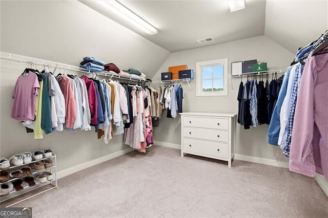 walk in closet with light colored carpet, vaulted ceiling, and visible vents