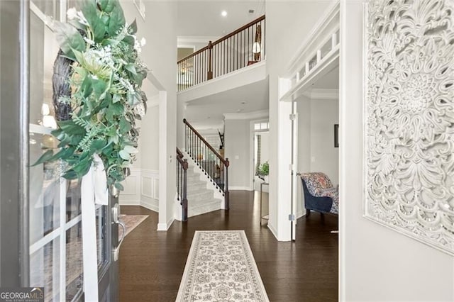 entryway featuring a towering ceiling, stairway, ornamental molding, dark wood-type flooring, and a decorative wall