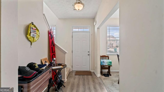 entrance foyer with arched walkways, a textured ceiling, baseboards, and wood finished floors