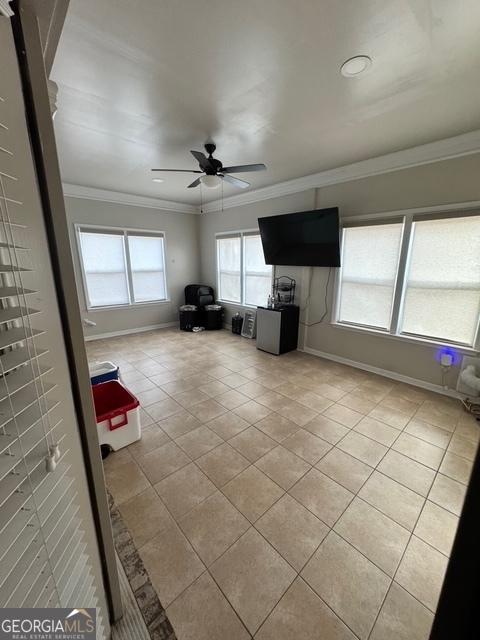 unfurnished living room with light tile patterned floors, ornamental molding, a ceiling fan, and baseboards