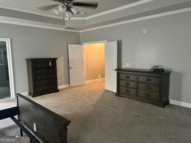 carpeted bedroom with a tray ceiling, crown molding, baseboards, and ceiling fan