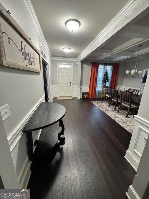 foyer with dark wood-style floors, a wainscoted wall, crown molding, a decorative wall, and a notable chandelier