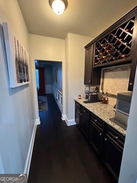 bar featuring dark wood-type flooring, backsplash, and baseboards