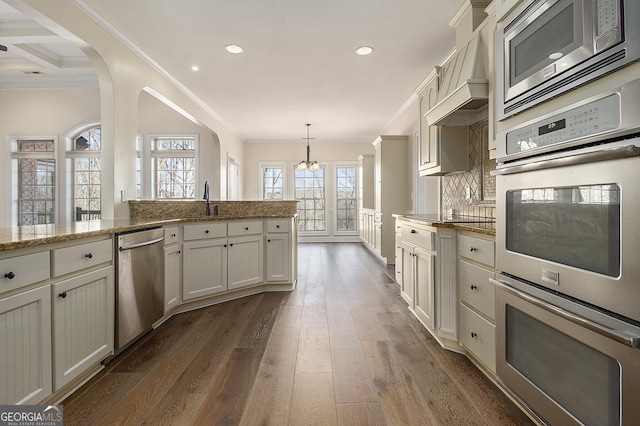 kitchen with dark wood-style floors, appliances with stainless steel finishes, ornamental molding, a sink, and premium range hood