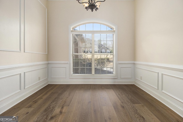 empty room featuring an inviting chandelier, a decorative wall, and dark wood-style flooring