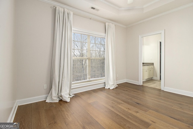 empty room with a raised ceiling, visible vents, crown molding, and wood finished floors