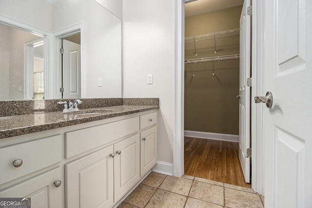 bathroom with a spacious closet, vanity, and baseboards