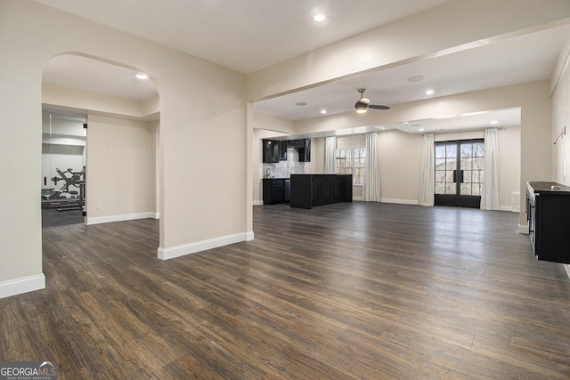 unfurnished living room with arched walkways, dark wood-style flooring, recessed lighting, a ceiling fan, and baseboards