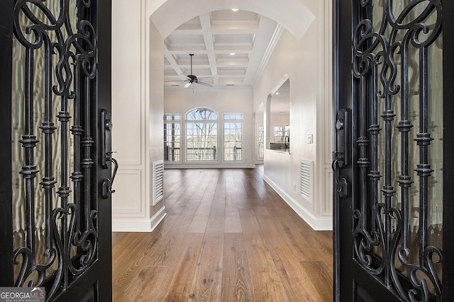 foyer entrance with arched walkways, coffered ceiling, ornamental molding, wood finished floors, and beamed ceiling