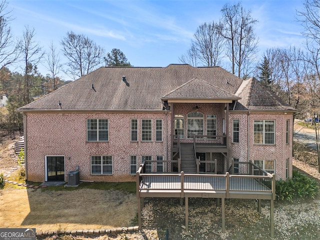 back of house featuring a shingled roof, brick siding, a wooden deck, and central air condition unit