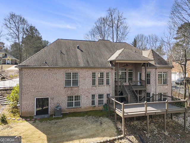 rear view of property with brick siding, roof with shingles, stairway, central AC, and a wooden deck