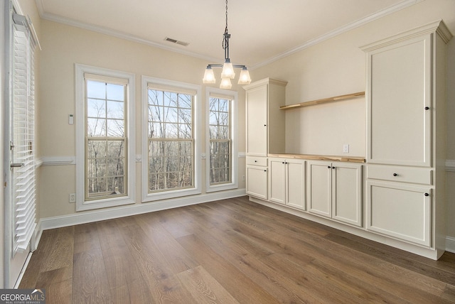 unfurnished dining area with baseboards, visible vents, dark wood finished floors, ornamental molding, and a notable chandelier