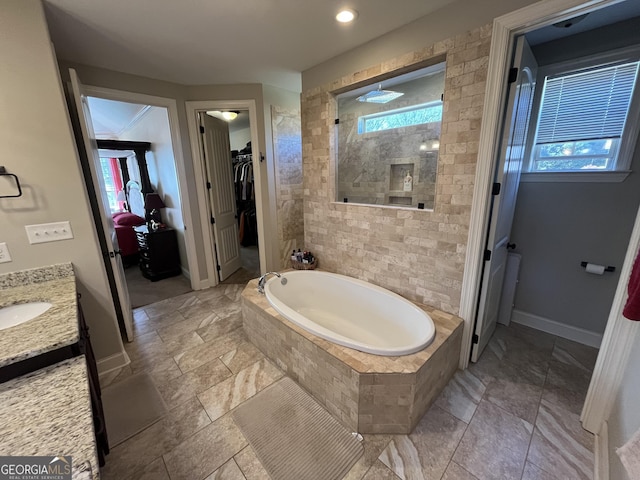 full bathroom with a walk in closet, a garden tub, vanity, baseboards, and walk in shower