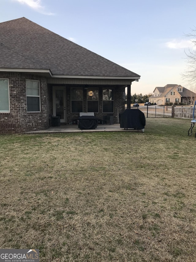 back of property with brick siding, a yard, roof with shingles, a patio area, and fence