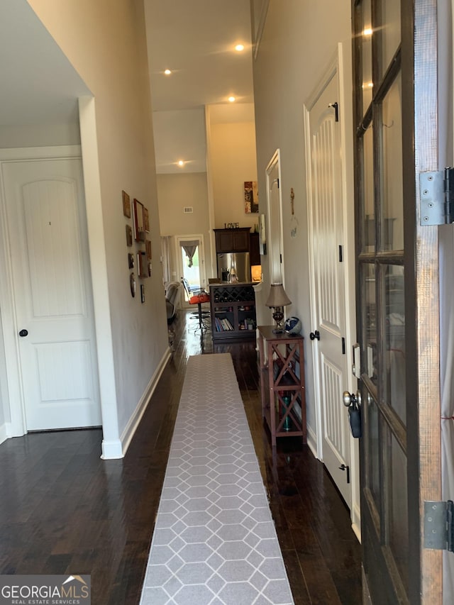 corridor featuring dark wood-style floors, a towering ceiling, and baseboards