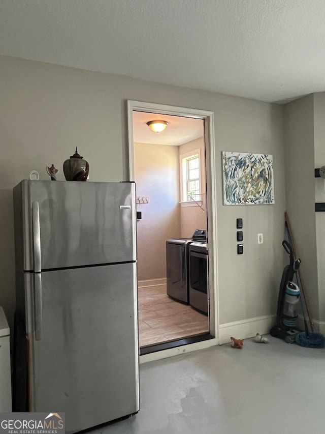 kitchen featuring freestanding refrigerator, baseboards, a textured ceiling, and washing machine and clothes dryer