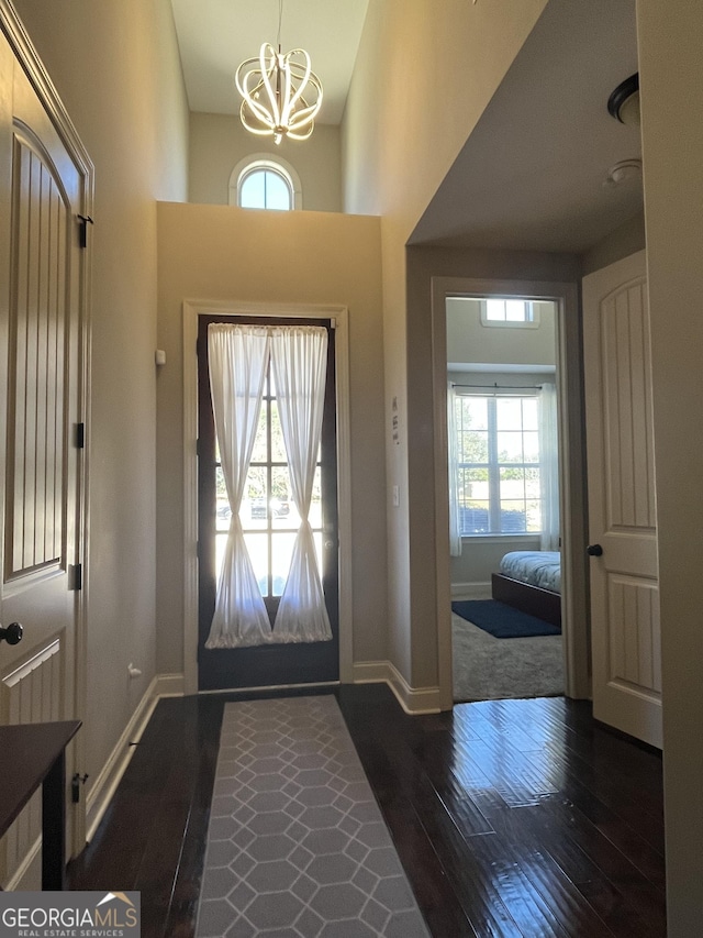 foyer featuring a high ceiling, a notable chandelier, dark wood finished floors, and baseboards