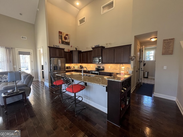 kitchen with a breakfast bar area, dark wood-type flooring, appliances with stainless steel finishes, light stone countertops, and tasteful backsplash