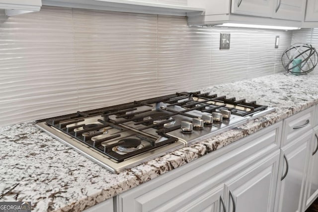 details featuring white cabinets, light stone countertops, stainless steel gas cooktop, and decorative backsplash