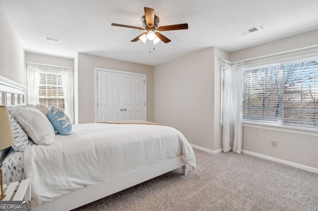 carpeted bedroom with a textured ceiling, a ceiling fan, visible vents, and baseboards