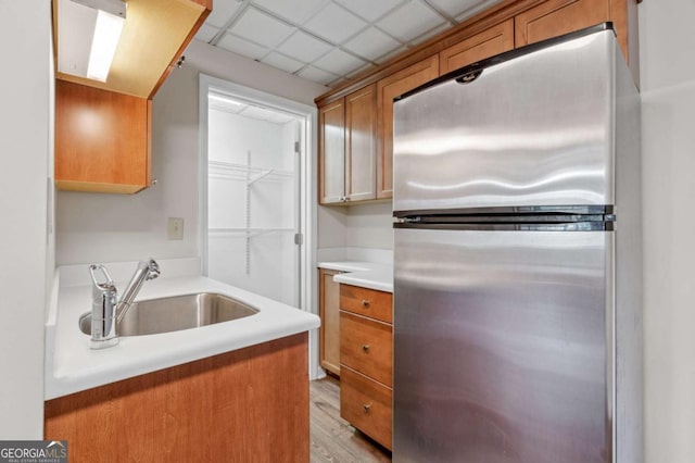 kitchen with a paneled ceiling, light countertops, light wood-style flooring, freestanding refrigerator, and a sink