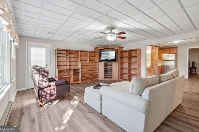 living room with a paneled ceiling, ceiling fan, baseboards, and wood finished floors