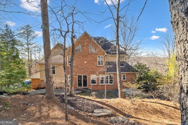 back of house with a chimney and brick siding