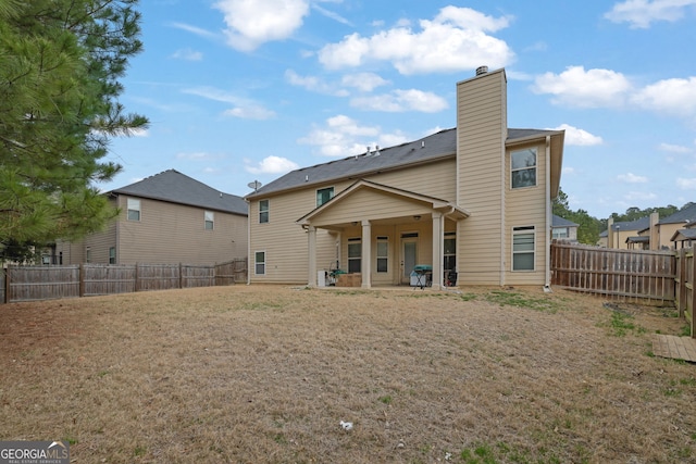 back of property with a fenced backyard, a yard, and a chimney