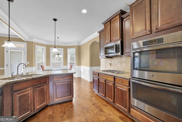 kitchen with a wainscoted wall, appliances with stainless steel finishes, decorative light fixtures, crown molding, and a sink