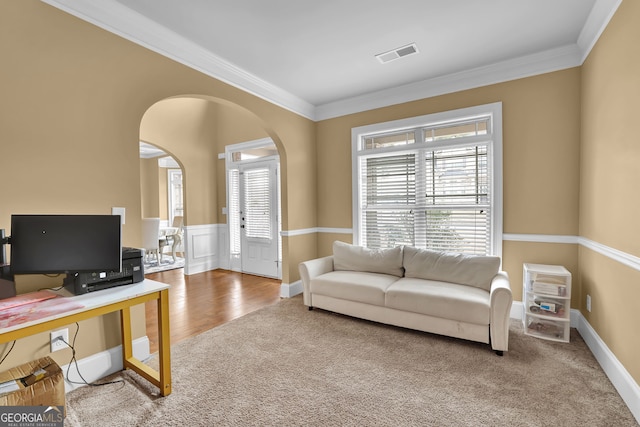 carpeted office space featuring arched walkways, wood finished floors, visible vents, ornamental molding, and wainscoting