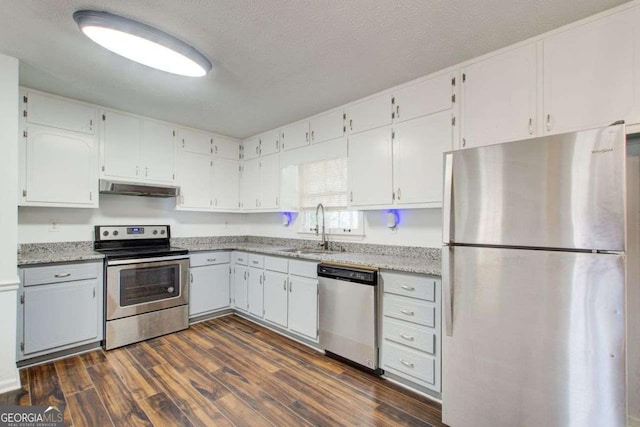 kitchen with white cabinets, dark wood finished floors, appliances with stainless steel finishes, under cabinet range hood, and a sink