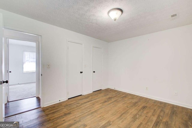 unfurnished bedroom featuring visible vents, a textured ceiling, baseboards, and wood finished floors