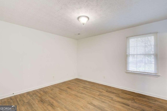 spare room featuring a textured ceiling, baseboards, and wood finished floors