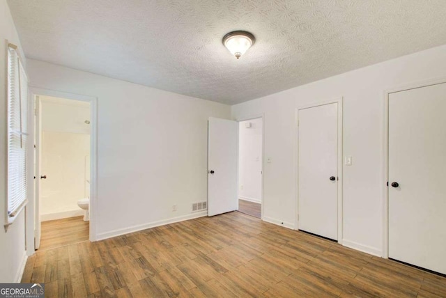 unfurnished bedroom with visible vents, a textured ceiling, ensuite bath, wood finished floors, and baseboards