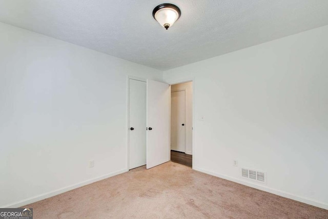 carpeted spare room with baseboards, visible vents, and a textured ceiling