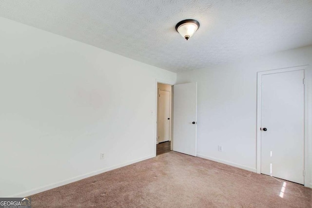 carpeted spare room featuring a textured ceiling and baseboards