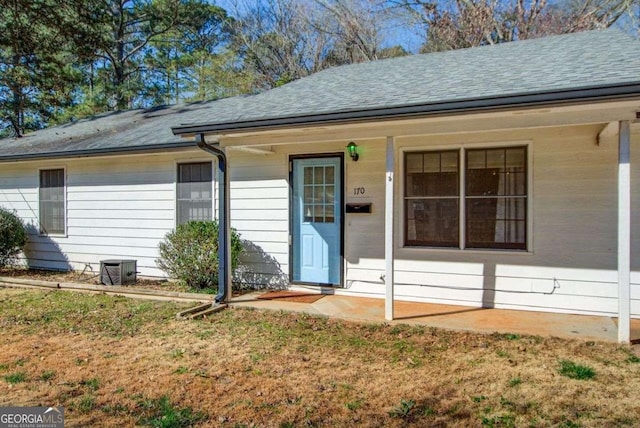 entrance to property with covered porch, a lawn, and roof with shingles