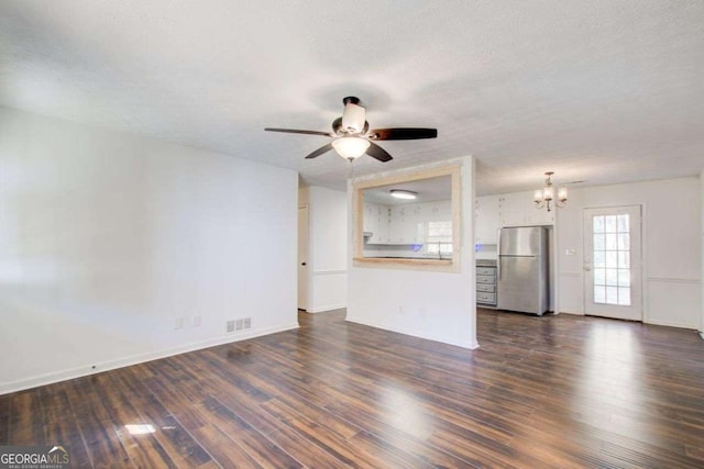 unfurnished living room featuring a textured ceiling, ceiling fan with notable chandelier, dark wood-type flooring, visible vents, and baseboards