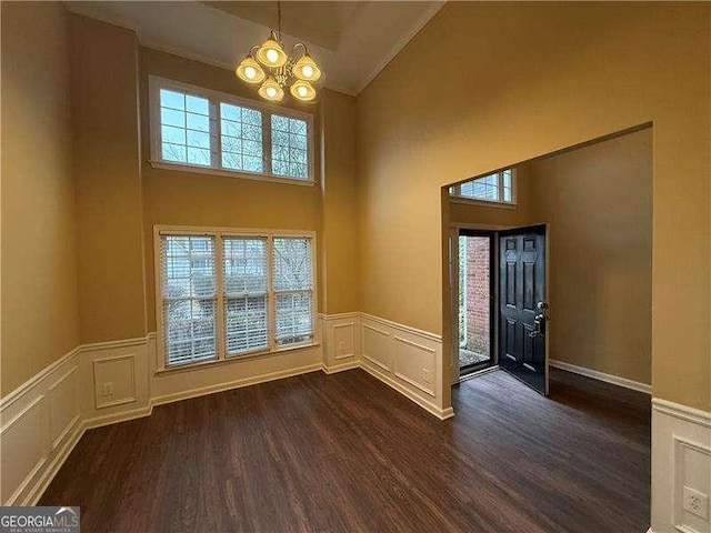 entrance foyer with a chandelier, dark wood-style flooring, plenty of natural light, and a wainscoted wall