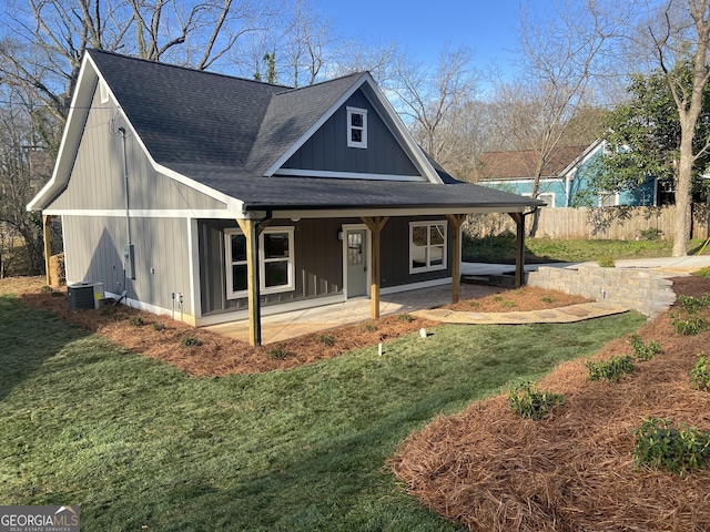 view of front of home with board and batten siding, a shingled roof, fence, central AC, and a front yard