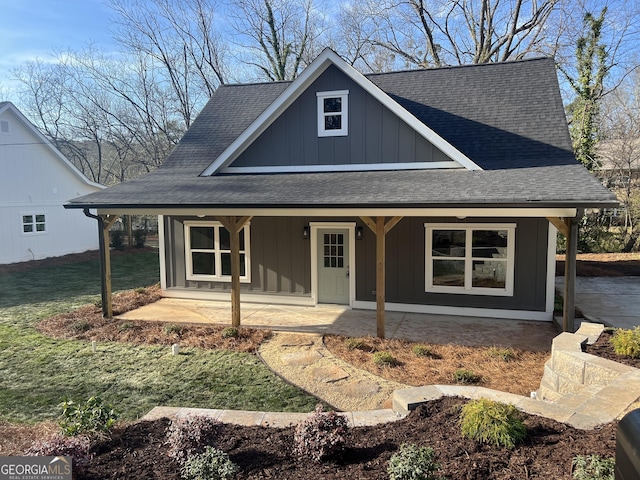 view of front of house with a shingled roof, board and batten siding, a porch, and a front lawn