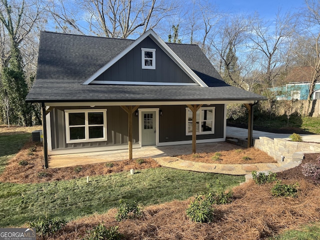 view of front facade featuring board and batten siding, cooling unit, covered porch, and a shingled roof