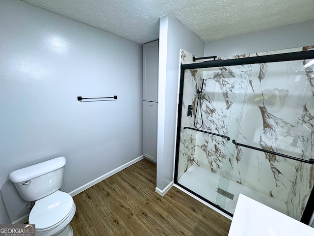 bathroom with a marble finish shower, baseboards, toilet, wood finished floors, and a textured ceiling