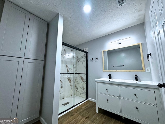 full bath featuring a textured ceiling, wood finished floors, visible vents, a marble finish shower, and double vanity