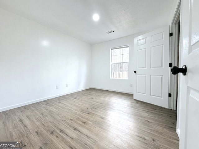 empty room featuring visible vents, a textured ceiling, baseboards, and wood finished floors