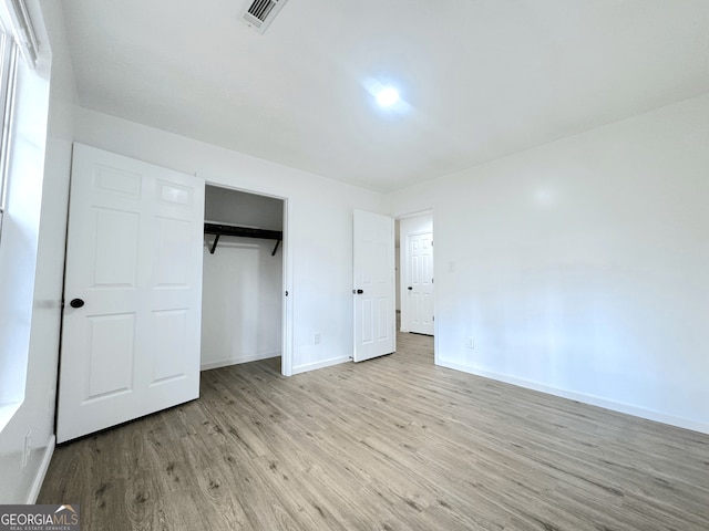 unfurnished bedroom featuring a closet, wood finished floors, visible vents, and baseboards