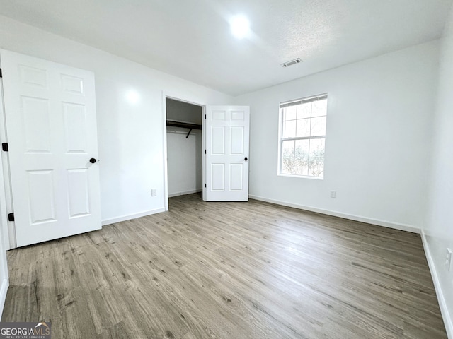 unfurnished bedroom featuring visible vents, a closet, baseboards, and wood finished floors