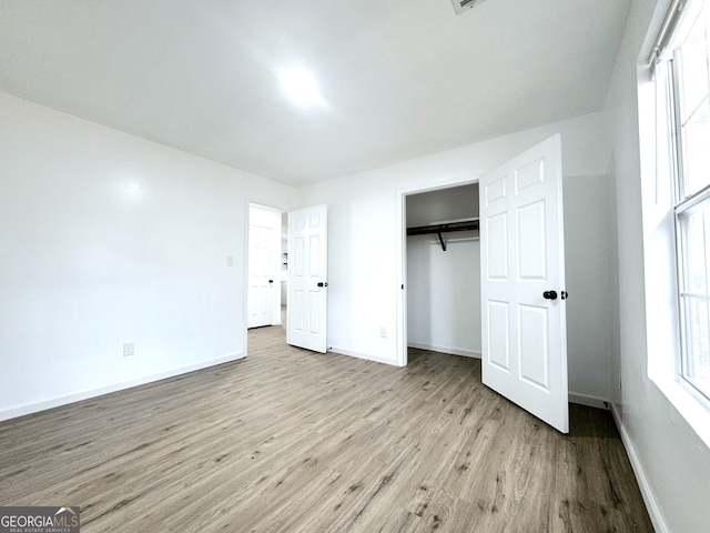 unfurnished bedroom featuring light wood finished floors, baseboards, and a closet